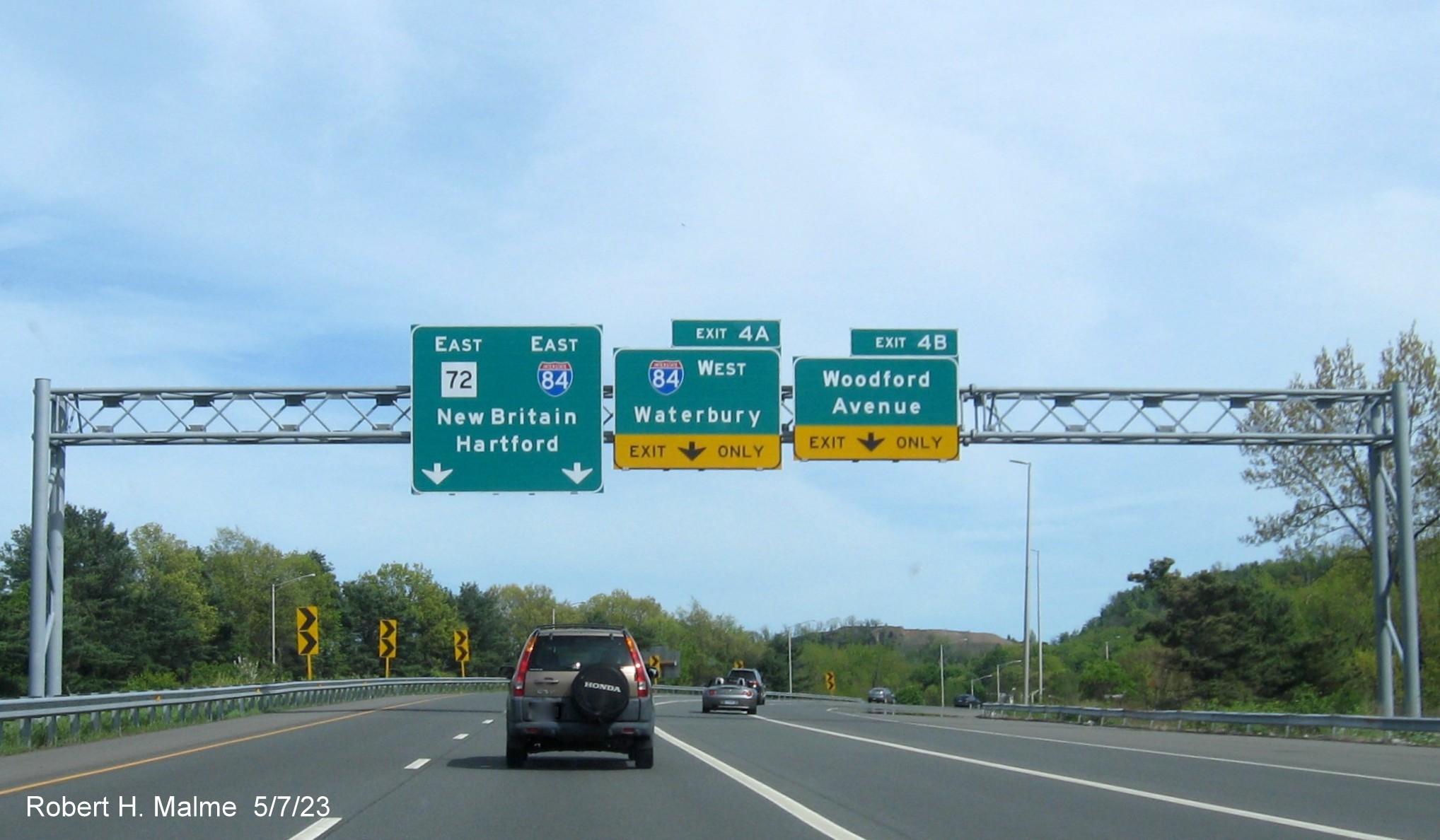 Image of overhead ramp sign for I-84 West/Woodford Avenue exits with new milepost based exit number and Old Exit 3-4 sign below on CT 72 East in Bristol, May 2023