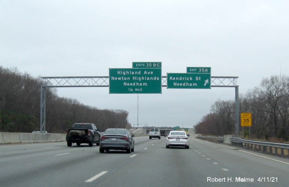 Image of overhead signs at ramp for Kendrick Street exit with new milepost 
                                            based exit numbers on I-95/MA 128 North in Needham, April 2021