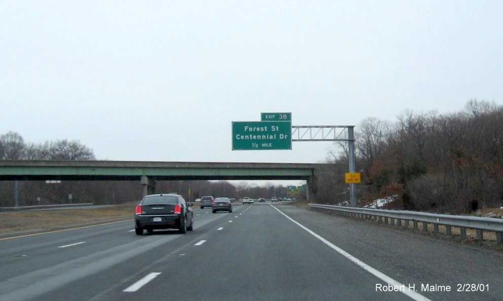 Image of 1/2 mile advance overhead sign for Forest Street/Centennial Drive exit with new milepost based exit number and yellow Old Exit Number sign on support post on MA 128 North in Peabody, February 2021