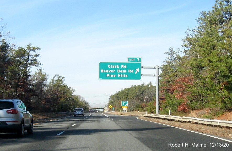 Image of overhead ramp sign for Clark Road exit with new milepost based exit number and gore sign with new number and yellow Old Exit number tab below on MA 3 North in Plymouth, December 2020