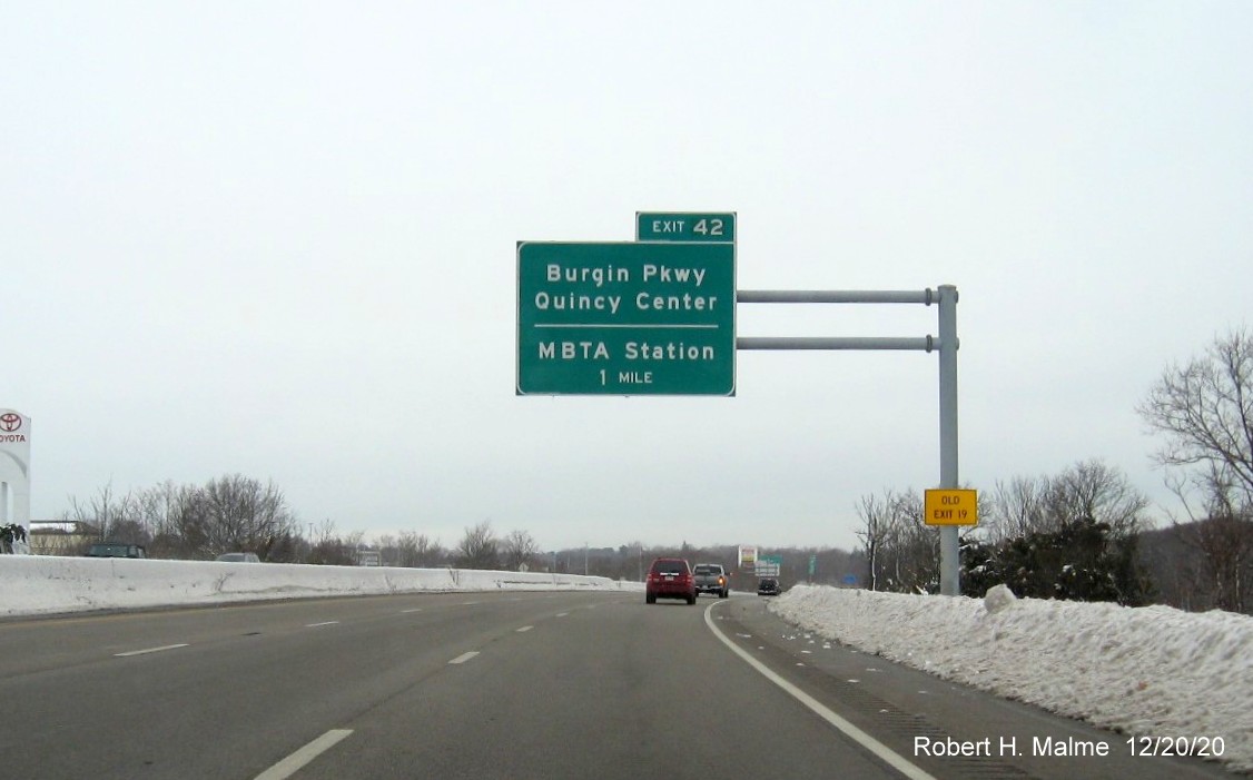 Image  of 1 mile advance overhead sign for Burgin Parkway exit with new milepost based exit number and yellow old exit number sign on support post on MA 3 North in Braintree, December 2020