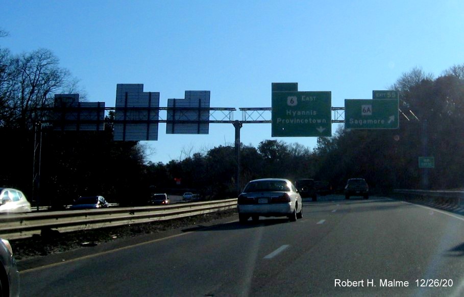 Image of overhead signs at ramp for MA 6A exit with new milepost based exit number and green old exit sign on right support post on US 6 East in Bourne, December 2020