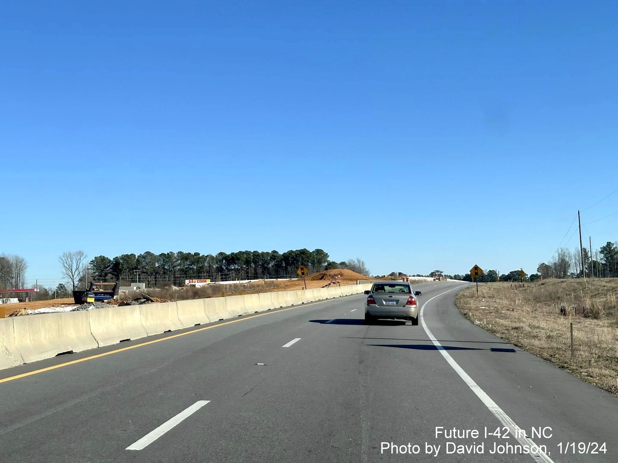 Image of traffic on US 70 East using future exit ramp for Wilson's Mills Road as temporary roadway
      through interchange work zone, photo by David Johnson, January 2024