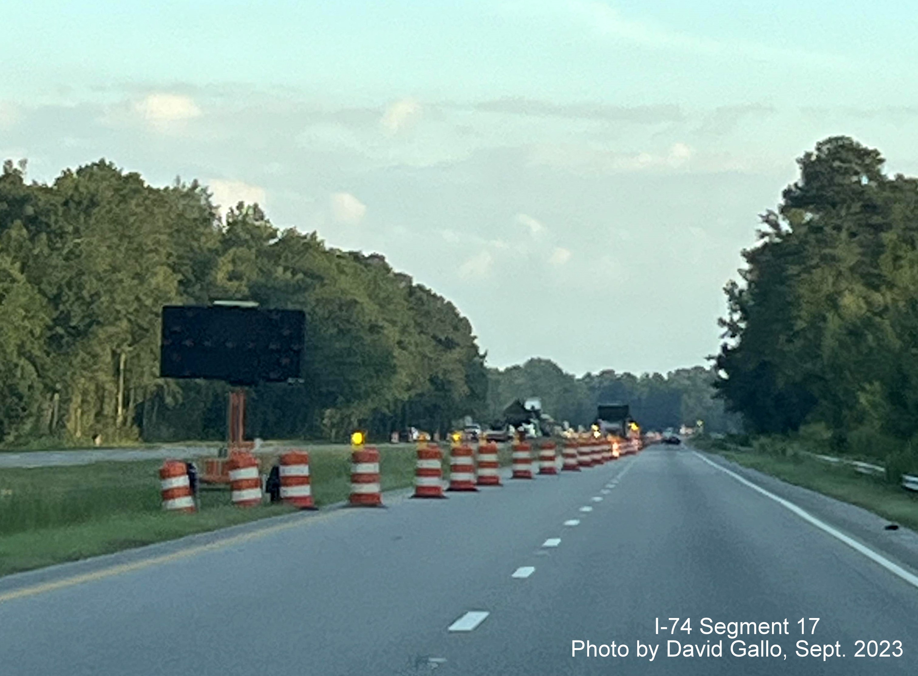 Image of construction barrels marking beginning of left lane closure approaching the NC 72 intersection on 
         US 74 West in interchange project work zone, David Gallo, September 2023
