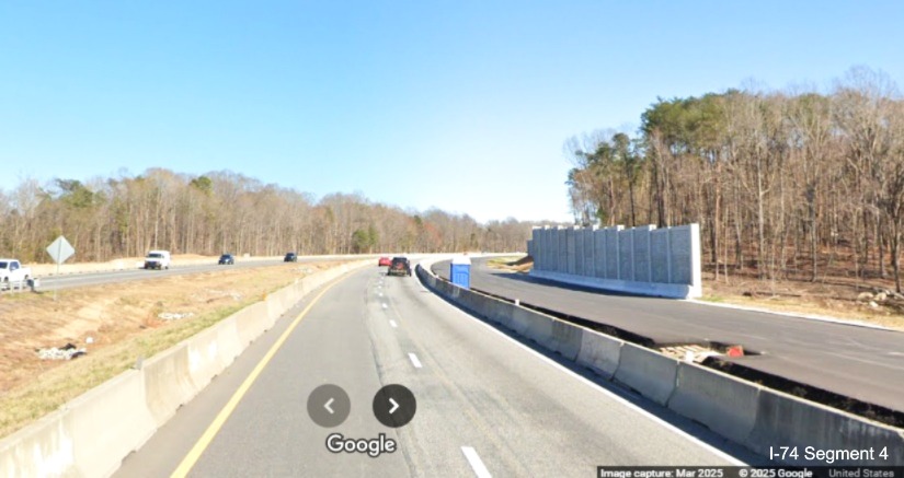 Image of paved future eastbound lanes and the start of completed noise wall beyond 
	  site of the future Winston-Salem Northern Beltway interchange on I-74 East, Google Maps Street View, March 2025