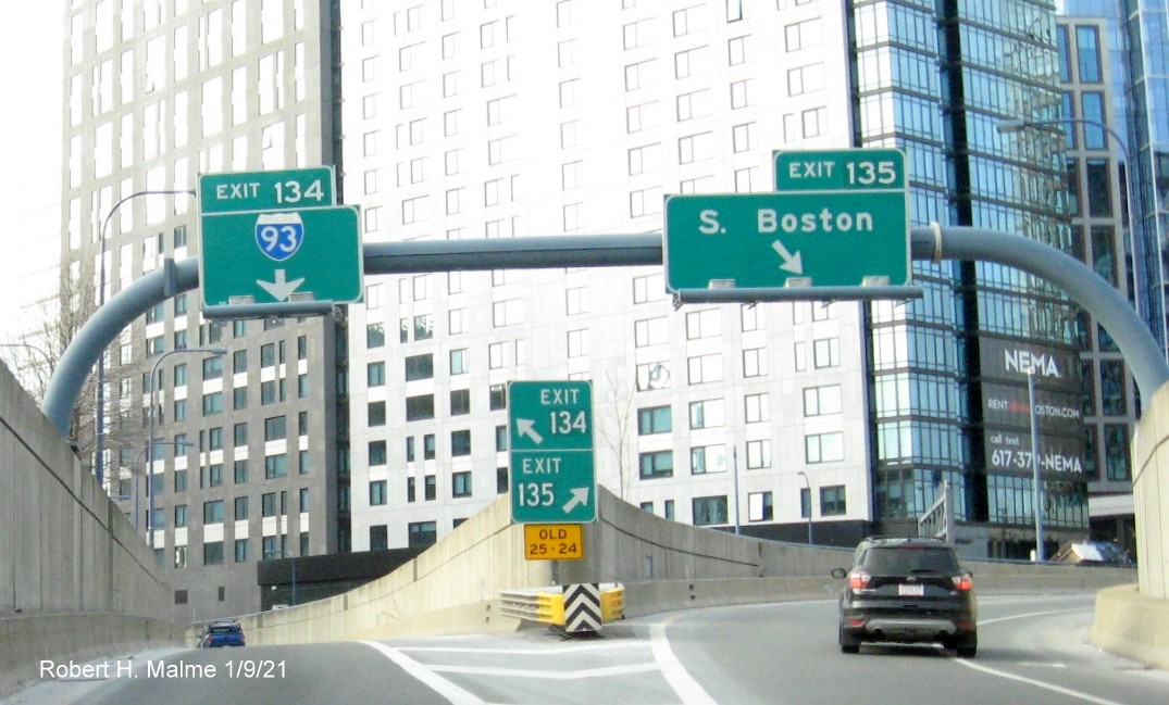 Image of overhead signs at split of I-93 and South Boston Exit ramps with new milepost based exit number and gore sign
                                       with yellow Old exit numbers sign below, January 2021