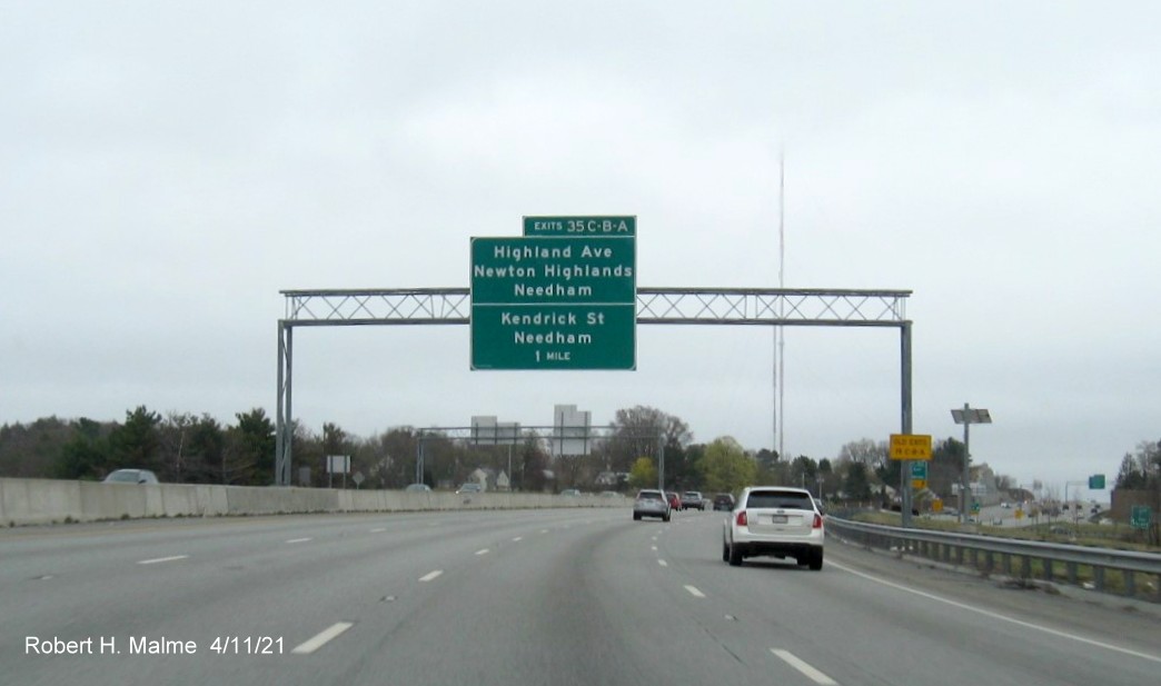 Image of 1 Mile advance overhead sign for Highland Avenue/Kendrick Street exits with new milepost based 
                                            exit numbers and yellow Old Exits 19 A-C advisory sign on right support on I-95/MA 128 South in Wellesley,                                             April 2021