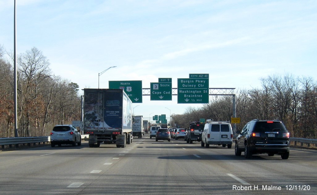 Image of overhead signs approaching split if I-93/US 1 North and MA 3 South ramps in Braintree showing new milepost based exit numbers on right sign with yellow old exit number sign on right support post, December 2020